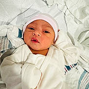 Amirah is registered to the contest to win money with this photo: newborn, baby, infant, clothing, hat, bed, blanket, towel, white, soft, cute, face, portrait, lying_down, indoors, closeup, person, sleepwear, wrapped, resting