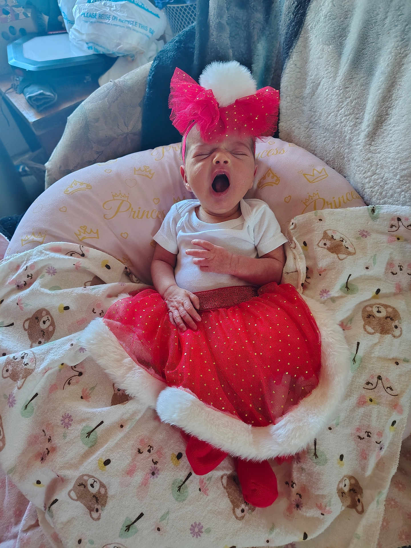 Roxanna is registered to the contest to win money with this photo: baby, infant, yawning, red_skirt, headband, pom_pom, blanket, bear_pattern, pink_pillow, princess_text, cozy, cute, sleepy, indoors, clothing, newborn, toddler, resting, soft, child