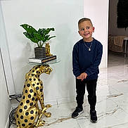 Evan participe au concours pour gagner de l'argent avec cette photo : child, boy, smiling, standing, indoor, plant, golden_cheetah, statue, table, books, dartboard, floor, marble_floor, wall, modern, casual_clothing, sneakers, necklace, decor, furniture