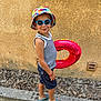 Evan participe au concours pour gagner de l'argent avec cette photo : child, boy, sunglasses, bucket_hat, swim_ring, summer, outdoor, side_view, smile, tank_top, shorts, sandals, curb, wall, dry_leaves, playful, sunny, casual, standing, fashion