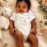 Mariah joined the competition — help win amazing prizes! baby, child, smiling, curly_hair, stuffed_animal, bunny, blanket, flowers, floral_arrangement, soft_texture, pastel_colors, onesie, cute, portrait, infant, happy, lying_down, cozy, indoor, skin