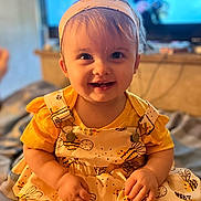 Cheyenne is registered to the contest to win money with this photo: baby, background_blur, bright, child, clothing, cute, face, happy, headband, headwear, indoor, infant, patterned_dress, person, portrait, sitting, smiling, warm_lighting, yellow_dress, young_child