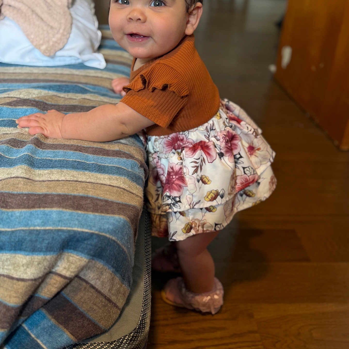 Shaddai joined the competition — help win amazing prizes! toddler, child, baby, smiling, standing, indoor, striped_blanket, floral_skirt, headband, wooden_floor, couch, clothing, footwear, face, person, cute, curious, home, furniture, portrait