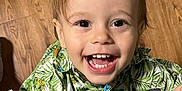 James is registered to the contest to win money with this photo: toddler, child, smiling, happy, face, eyes, mouth, teeth, hair, shirt, patterned_clothing, tropical, leaf_pattern, indoor, wooden_floor, person, joy, cute, portrait, closeup