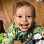 toddler, child, smiling, happy, face, eyes, mouth, teeth, hair, shirt, patterned_clothing, tropical, leaf_pattern, indoor, wooden_floor, person, joy, cute, portrait, closeup
