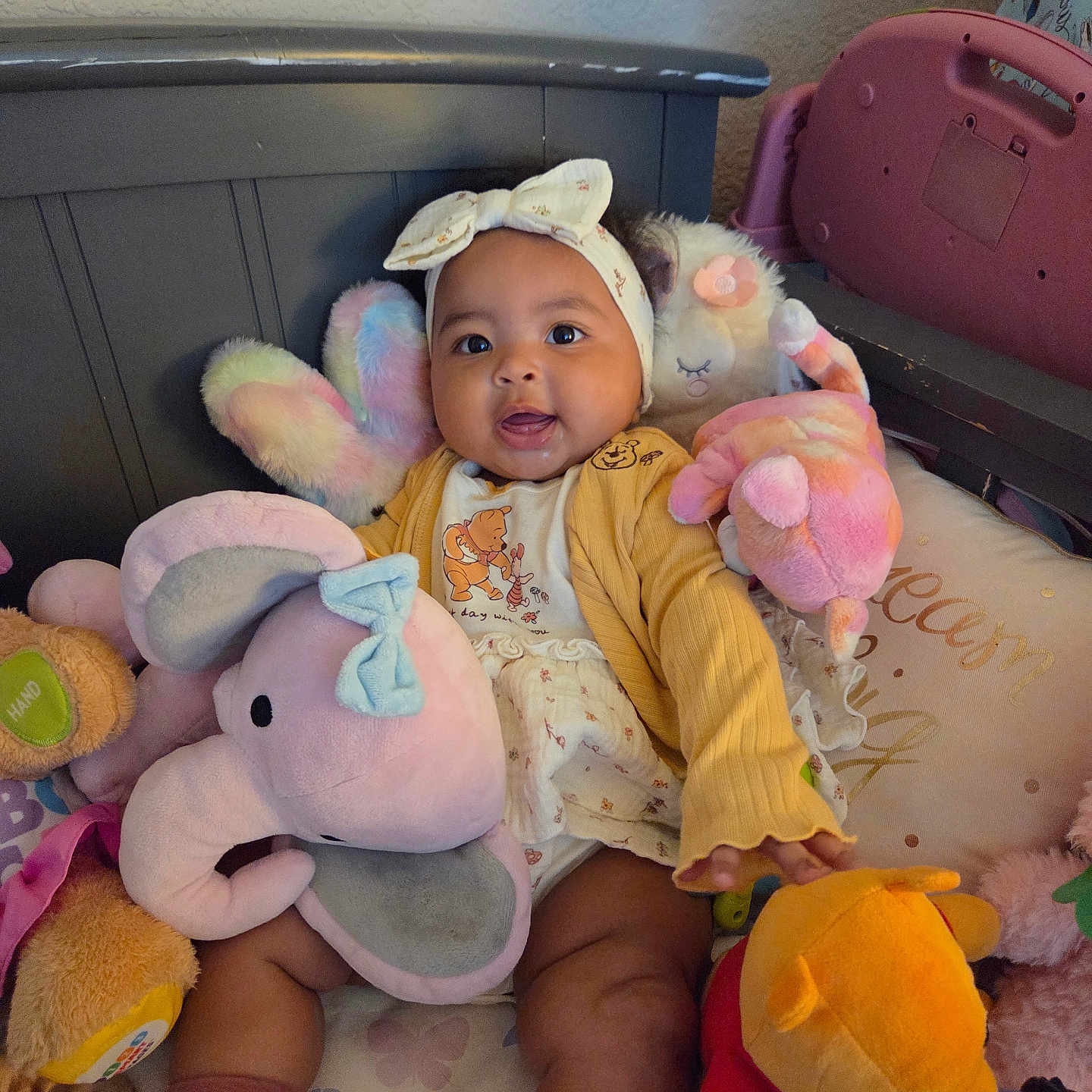 Iniah joined the competition — help win amazing prizes! baby, child, infant, smiling, sitting, portrait, headband, bow, onesie, clothing, stuffed_animal, plush_toy, elephant_toy, teddy_bear, winnie_the_pooh, crib, bedding, nursery, indoors, colorful