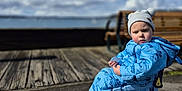 Mateo joined the competition — help win amazing prizes! child, toddler, beanie, puffer_jacket, blue_jacket, toy_cart, wheels, sneakers, pavement, boardwalk, bench, waterfront, sea, clouds, sky, outdoors, portrait, sitting, expression, cold_weather