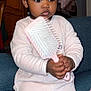 toddler, child, hairbrush, pink, hair_ties, sitting, couch, indoor, clothing, long_sleeves, furniture, expressionless, person, baby, black_hair, curly_hair, wooden_cabinet, stroller, toy, home