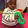 Nehelah participe au concours pour gagner de l'argent avec cette photo : toddler, child, toy, green_toy, headband, pink_headband, striped_sweater, sweater, red_basket, playmat, indoor, curious, sitting, person, young_child, clothing, hand, face, black_hair, playroom