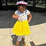 child, girl, birthday, yellow_skirt, sandals, sunlight, shadow, tiara, braids, outdoor, concrete, celebration, dress, white_tights, person, happy, beads, headwear, fashion, casual