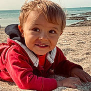 Ruben a rejoint le concours — aidez-le/la à gagner de superbes lots ! child, toddler, beach, sand, ocean, water, rocks, smile, red_jacket, outdoor, sunlight, happy, portrait, face, hands, casual_clothing, nature, daytime, seaside, young_child
