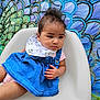baby, child, denim_dress, bib, chair, colorful_background, peacock_feathers, mural, portrait, indoor, cute, infant, sitting, person, skin, hair, expression, clothing, hand, face