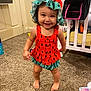 Alayna joined the competition — help win amazing prizes! toddler, child, smiling, watermelon_hat, orange_dress, barefoot, carpet, nursery, baby, clothing, indoor, person, cute, happy, toy, crib, diapers, room, standing, young_child