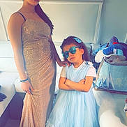 Louane participe au concours pour gagner de l'argent avec cette photo : two_people, girl, child, dress, gown, sunglasses, indoor, living_room, fashion, pose, standing, furniture, toy, casual, home, floor, curtain, hair, smile, person