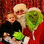child, toddler, santa_claus, grinch, christmas_tree, holiday, festive, costume, decorations, fireplace, stockings, smile, portrait, indoor, celebration, red, green, fur_coat, gloves, face