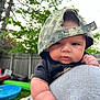 baby, child, face, cap, hat, outdoor, greenery, backyard, fence, person, shoulder, skin, cute, infant, portrait, casual, daylight, expression, headwear, closeup