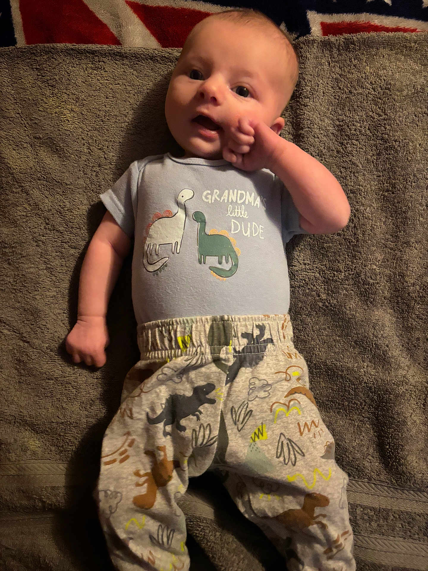Bobby joined the competition — help win amazing prizes! baby, infant, towel, clothing, dinosaur, pattern, cute, lying_down, person, child, apparel, fabric, hand, face, expression, indoor, text, sleepwear, soft_texture, union_jack