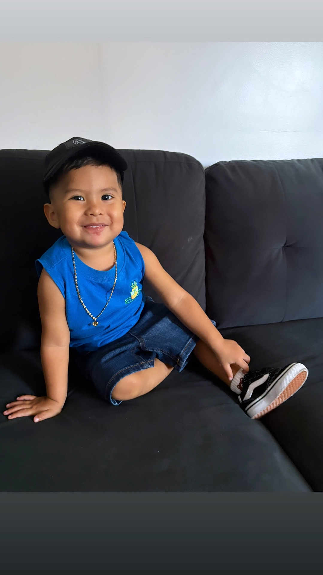 Eiden joined the competition — help win amazing prizes! child, smiling, sitting, couch, blue_shirt, denim_shorts, cap, necklace, shoe, indoors, happy, portrait, casual, young_child, black_couch, comfortable, cute, fashion, relaxed, person