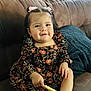 toddler, child, smiling, sitting, couch, blanket, cookie, hair_bows, floral_dress, indoor, happy, cute, person, portrait, cozy, furniture, socks, brown, knitted, snack