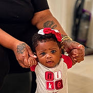 Kailani is registered to the contest to win money with this photo: baby, child, infant, person, hands, tattoo, bracelet, bow, headwear, clothing, nike, red, white, black_shirt, indoor, floor, expression, supporting_hands, cute, portrait