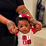 baby, child, infant, person, hands, tattoo, bracelet, bow, headwear, clothing, nike, red, white, black_shirt, indoor, floor, expression, supporting_hands, cute, portrait