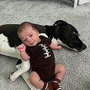 Liam joined the competition — help win amazing prizes! baby, infant, dog, black_and_white_dog, carpet, onesie, socks, football_theme, crib, diapers, floor, pet, child, lying_down, indoor, cute, animal, person, resting, smiling