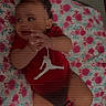 Hermayia is registered to the contest to win money with this photo: baby, infant, red_bow, red_onesie, socks, floral_blanket, lying_down, clothing, cute, child, portrait, indoors, person, adorable, hands, face, head, looking_away, baby_clothes, soft_surface