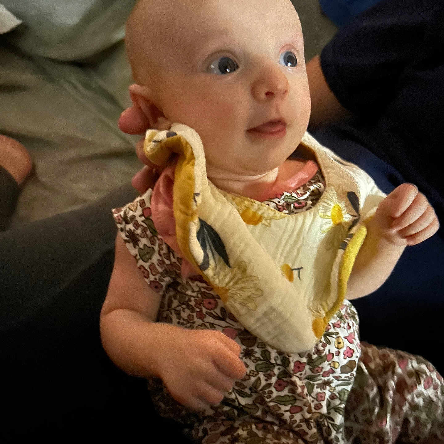 Marliese is registered to the contest to win money with this photo: baby, bib, candid, child, curious_expression, cute, eyes, fabric, face, floral_clothing, hand, head, holding, indoor, infant, person, portrait, seated, skin, sleeveless