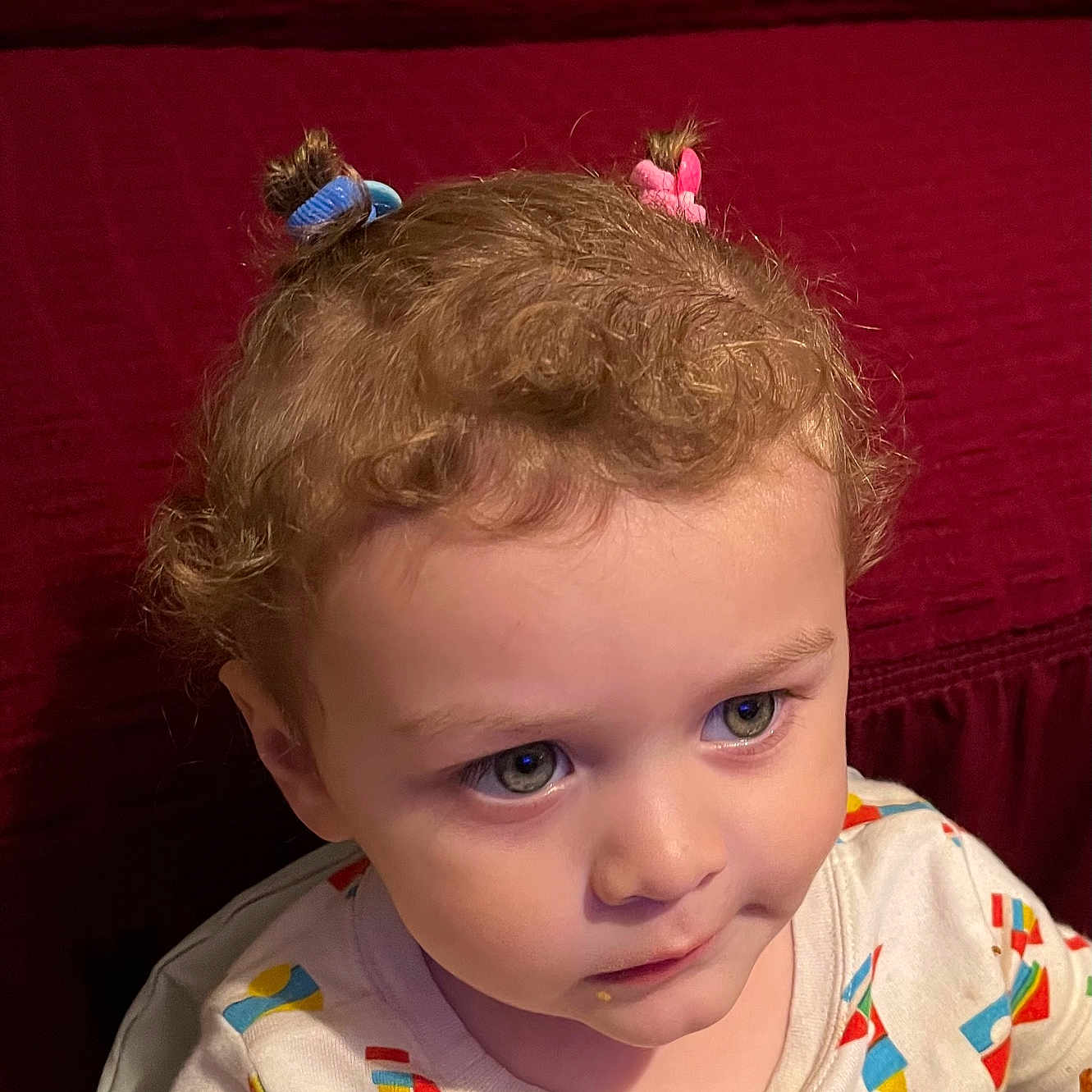 Nikolai joined the competition — help win amazing prizes! toddler, child, face, hair_ties, curly_hair, colorful_clothing, patterned_shirt, indoor, portrait, looking_away, expression, cute, young_child, person, sitting, closeup, red_background, soft_lighting, casual, innocent