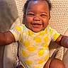 baby, infant, child, smiling, happy, portrait, closeup, face, sitting, indoors, onesie, lemon_pattern, yellow, cushion, blanket, chair, curly_hair, dark_skin, adorable, photography