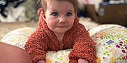 Kinzley joined the competition — help win amazing prizes! baby, child, pillow, fuzzy_jacket, curious, indoor, bed, floral_pattern, person, young_child, soft_texture, hands, face, blue_eyes, background_blur, cozy, casual, expression, candid, home