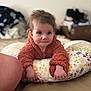 baby, child, pillow, fuzzy_jacket, curious, indoor, bed, floral_pattern, person, young_child, soft_texture, hands, face, blue_eyes, background_blur, cozy, casual, expression, candid, home
