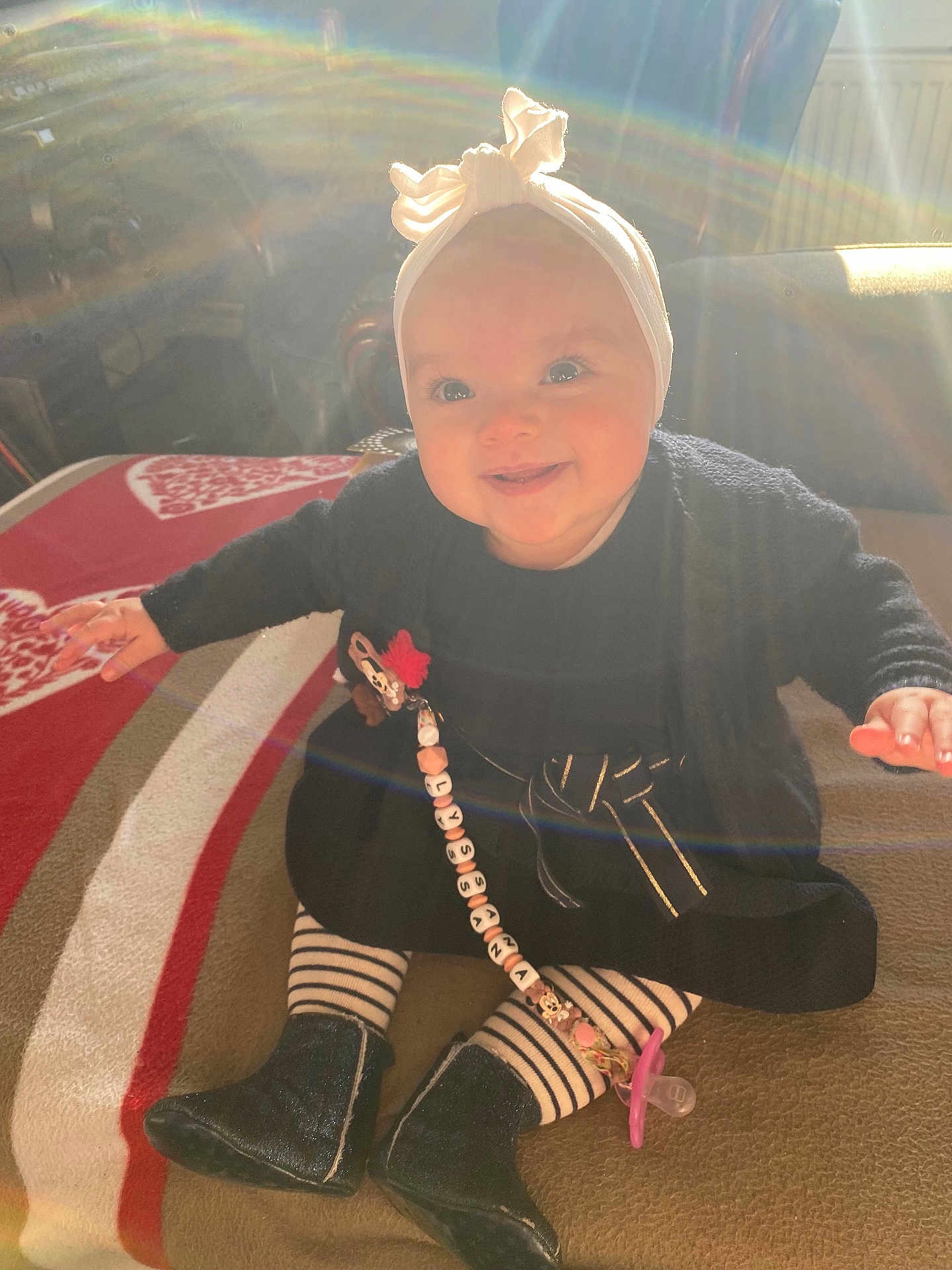 Lyssana participe au concours pour gagner de l'argent avec cette photo : baby, beaded_clip, blanket, boots, bow, child, cozy, cute, dress, happy, headband, indoor, lens_flare, pacifier, person, sitting, smiling, striped_tights, sunlight, warm