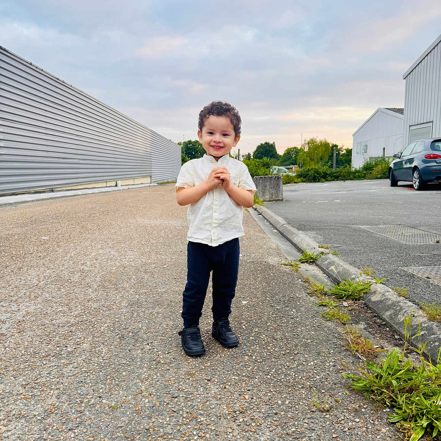Ryel a rejoint le concours — aidez-le/la à gagner de superbes lots ! asphalt, car, casual_clothing, child, cloudy_sky, curb, curly_hair, greenery, industrial_building, outdoor, pants, plants, road, shirt, shoes, sidewalk, smiling, standing, urban, young_child
