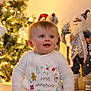 Theo is registered to the contest to win money with this photo: baby, celebration, child, christmas, christmas_tree, cute, decorations, festive, happy, holiday, indoors, lights, pajamas, portrait, reindeer, santa_figure, seasonal, sitting, smiling, white_clothing