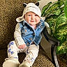 baby, child, smile, hat, denim_vest, floral_pants, shoes, chair, leopard_print, indoor, plant, greenery, cute, portrait, seated, happy, face, clothing, infant, cozy
