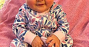 Zelda is registered to the contest to win money with this photo: baby, child, smiling, onesie, pink_blanket, indoor, cute, infant, sitting, hand, foot, patterned_clothing, cushion, animal_print, cozy, portrait, happy, soft_texture, person, face