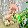 Zelda is registered to the contest to win money with this photo: baby, child, infant, onesie, leaf, plant, greenery, chair, cushion, indoor, curious, blue_eyes, bald, cute, sitting, hand, mouth, soft_light, home, portrait