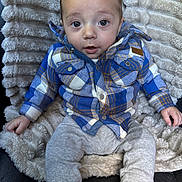 Wesley is registered to the contest to win money with this photo: baby, child, plaid_shirt, gray_pants, blanket, soft_texture, seated, indoor, cute, curious, face, head, hands, legs, cozy, casual_clothing, infant, portrait, comfortable, cute_expression