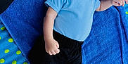 Wesley is registered to the contest to win money with this photo: baby, blue_shirt, black_shorts, blue_towel, polka_dot_blanket, rocks, infant, barefoot, outdoor, portrait, lying_down, serious_expression, child, person, skin, head, hand, foot, clothing, texture