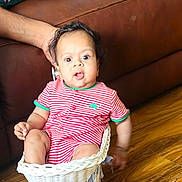 Kailan joined the competition — help win amazing prizes! baby, infant, child, striped_clothing, wicker_basket, furniture, brown_couch, wooden_floor, hand, indoor, colorful_pillow, toy_cart, cute, seated, expression, living_room, person, supporting_hand, casual, home
