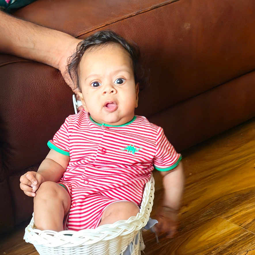 Kailan joined the competition — help win amazing prizes! baby, brown_couch, casual, child, colorful_pillow, cute, expression, furniture, hand, home, indoor, infant, living_room, person, seated, striped_clothing, supporting_hand, toy_cart, wicker_basket, wooden_floor