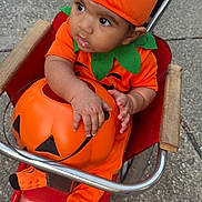 Carlos is registered to the contest to win money with this photo: baby, pumpkin_costume, orange_clothing, jack_o_lantern, stroller, child, halloween, outdoor, curious, drool, red_stroller, socks, green_leaf_collar, costume_hat, cute, person, infant, seasonal, holiday, festive