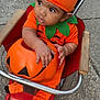baby, pumpkin_costume, orange_clothing, jack_o_lantern, stroller, child, halloween, outdoor, curious, drool, red_stroller, socks, green_leaf_collar, costume_hat, cute, person, infant, seasonal, holiday, festive