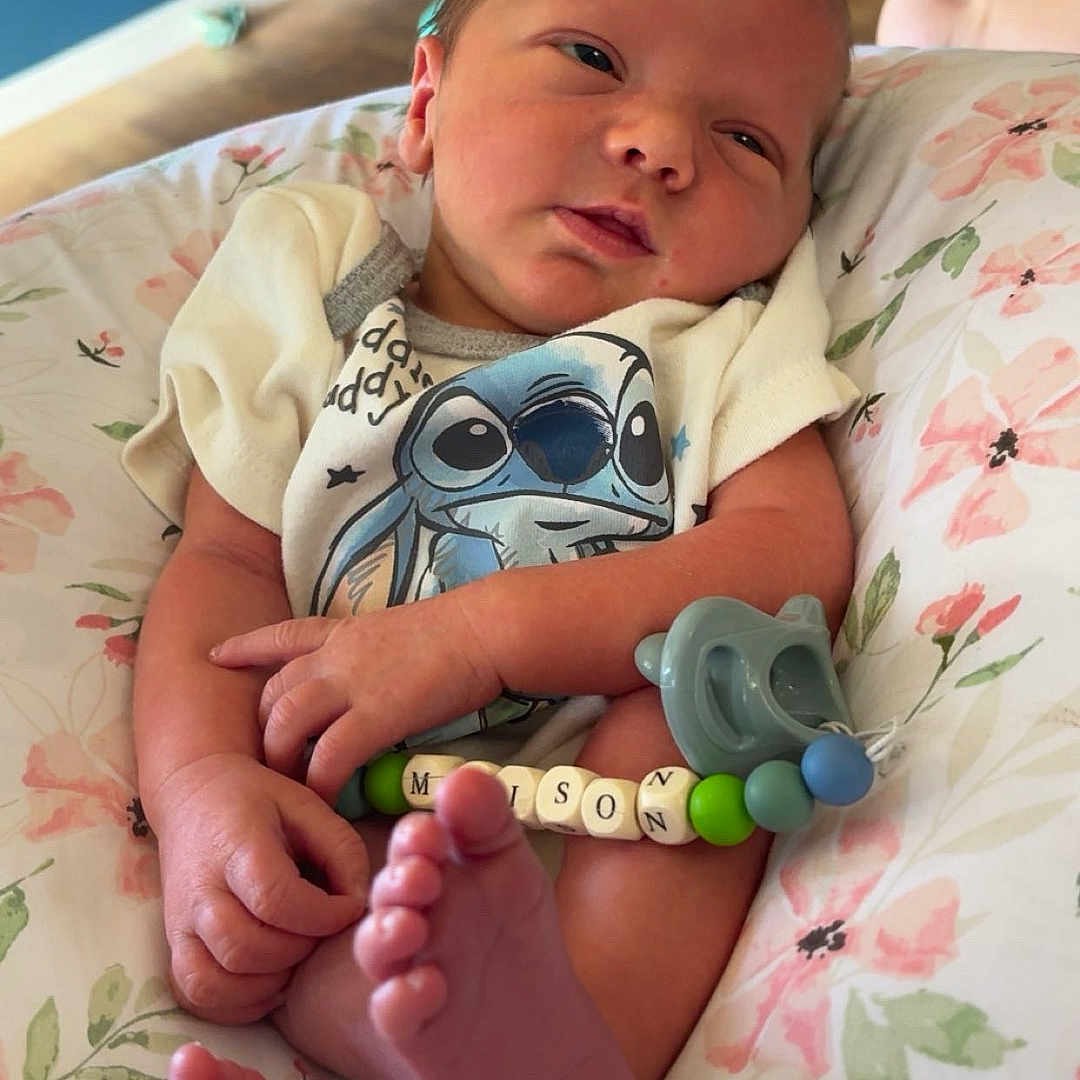 Maison is registered to the contest to win money with this photo: baby, bedroom, child, clothing, cushion, cute, face, floral, foot, hand, home, indoors, infant, newborn, onesie, pacifier, person, resting, sleepy, wooden_floor