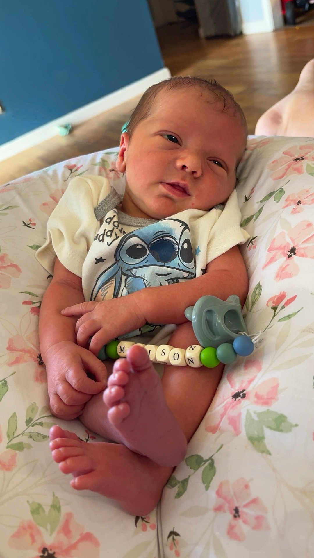 Maison is registered to the contest to win money with this photo: newborn, baby, infant, pacifier, onesie, clothing, hand, foot, face, person, cushion, floral, bedroom, wooden_floor, indoors, cute, sleepy, resting, child, home