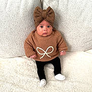 Layana a rejoint le concours — aidez-le/la à gagner de superbes lots ! baby, child, knitwear, headband, bow, sweater, black_pants, white_socks, couch, cushion, soft_texture, indoor, portrait, cute, infant, seated, looking_at_camera, cozy, warm_clothing, neutral_colors