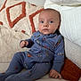 baby, infant, blue_onesie, couch, pillows, texture, pattern, cute, portrait, indoor, child, soft_furniture, relaxed, wide_eyes, seated, cozy, home, comfort, expression, small_hand