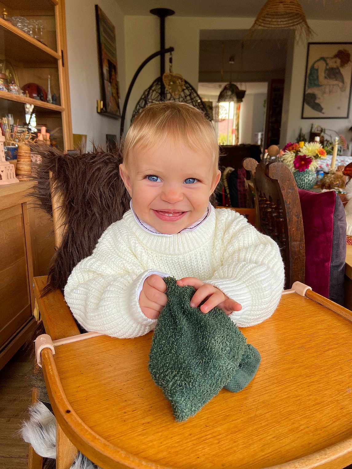 Asmaa a rejoint le concours — aidez-le/la à gagner de superbes lots ! toddler, child, smile, blue_eyes, high_chair, wooden_furniture, green_cloth, white_sweater, indoor, flowers, decor, room, chair, table, portrait, happy, person, baby, cute, cozy