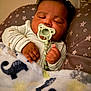 baby, pacifier, sleeping, blanket, animal_print, cushion, stars, infant, cozy, hands, clothing, bedtime, portrait, cute, indoors, rest, child, soft_texture, comfort, relaxation